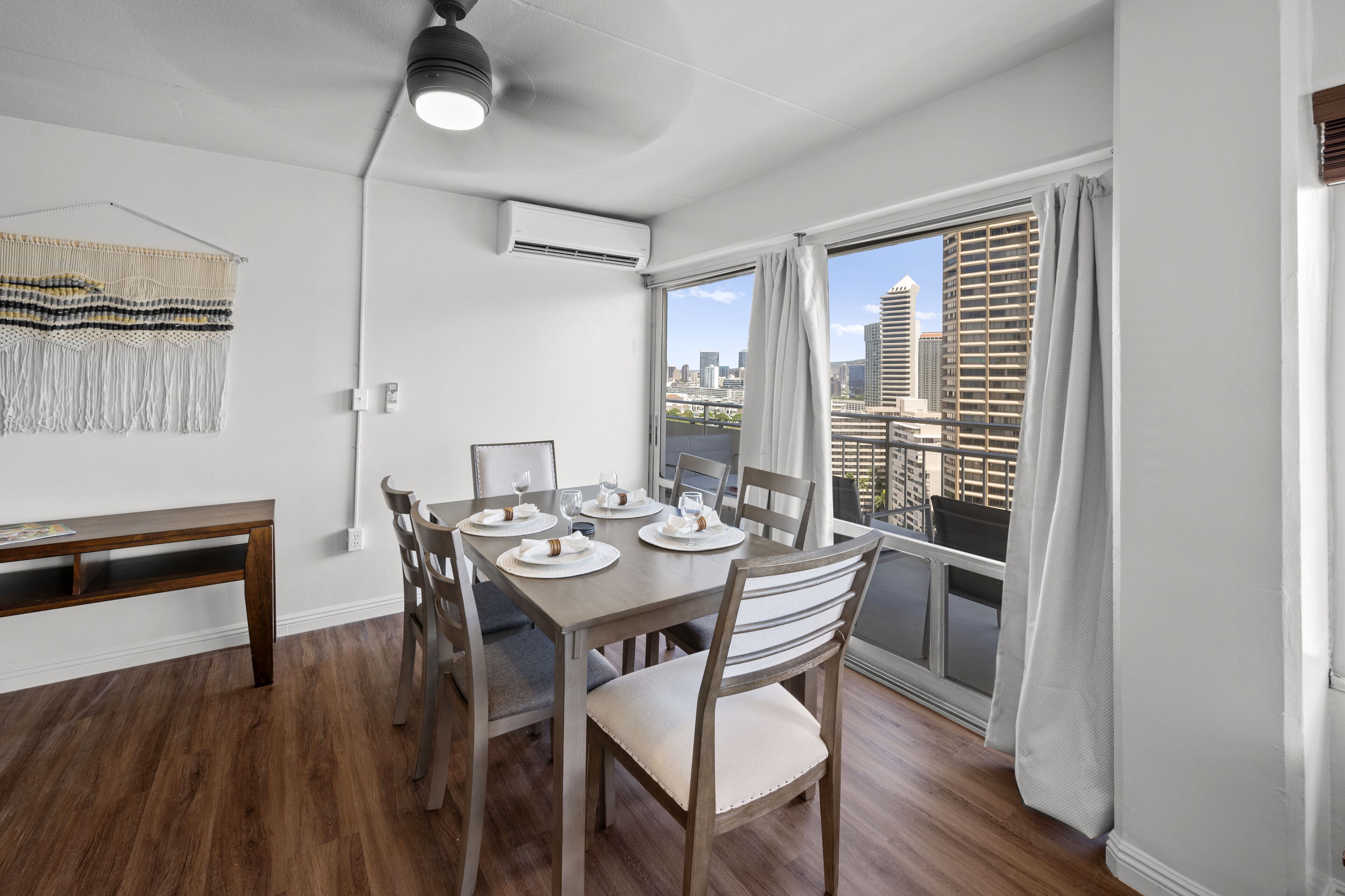 Un comedor con una mesa dispuesta para cuatro, una banca y vistas de la ciudad a través de un ventanal.
