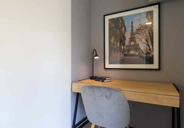 Un escritorio con un cuadro enmarcado de la Torre Eiffel, una lámpara y una silla.