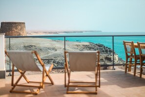 Un balcone con due sedie di legno affacciato su una costa rocciosa e una vista limpida sul mare.