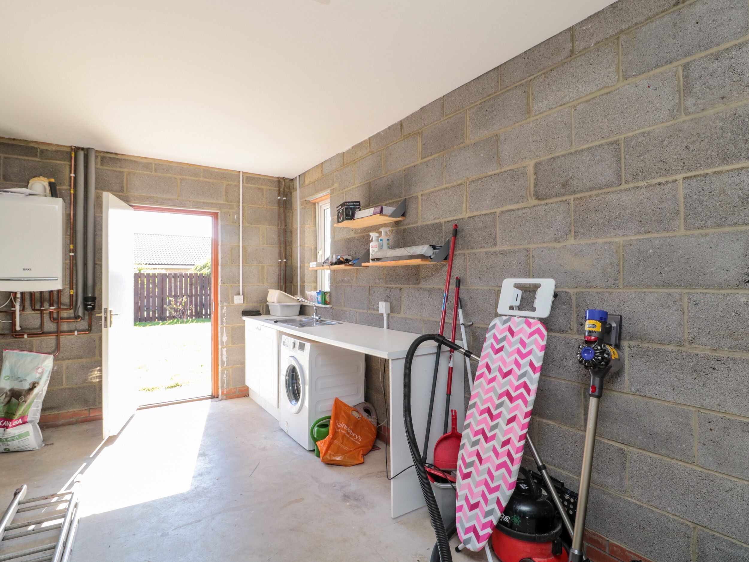 A laundry room with a washing machine, drying rack, ironing board, and ironing board stand.
