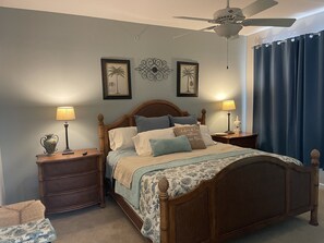 A bedroom with a wooden bed, two nightstands, a ceiling fan, and decorative wall art. - Condo in Quarry Resort Community (Naples)