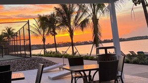Eine Terrasse mit Sitzgelegenheiten, Blick auf den Sonnenuntergang über dem Wasser und Palmen.