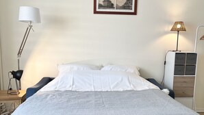 A neatly made bed with a grey bedspread, a white pillow, and a headboard. There is a framed picture on the wall above the bed. - Escale en Duo, studio Plage d'Opale sea view +wifi (Neufchâtel-Hardelot)