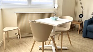 A modern living room with a white table, two beige chairs, a blue sofa, a floor lamp, and a radiator. - Escale en Duo, studio Plage d'Opale sea view +wifi (Neufchâtel-Hardelot)