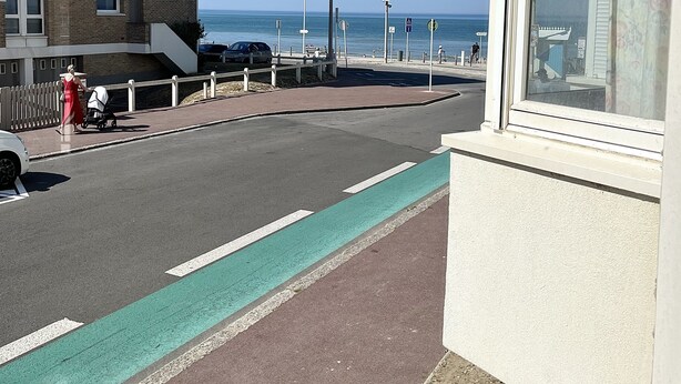 A coastal street with a pedestrian path, a parked car, and a building with a visible balcony. - Escale en Duo, studio Plage d'Opale sea view +wifi (Neufchâtel-Hardelot)