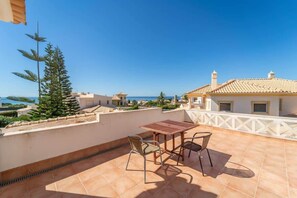 Eine Terrasse mit Tisch und Stühlen mit Blick auf eine Küstenlandschaft, einschließlich Gebäude und klarem Himmel.