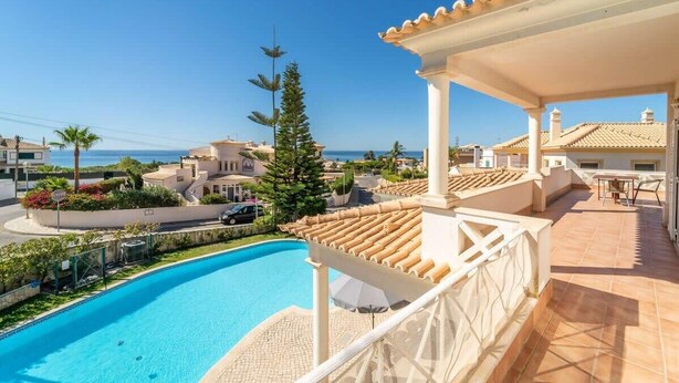 En swimmingpool med udsigt over havet, en overdækket terrasse og et boligområde.