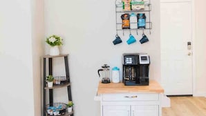 Een kitchenette met een koffiezetapparaat, een plank met planten en een hangende organizer met mokken.