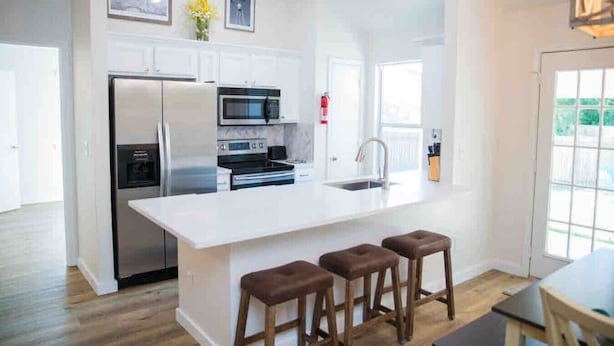 Een moderne keuken met witte kasten, roestvrijstalen apparatuur en een groot eiland met krukken.