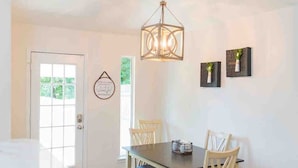 Een eetgedeelte met een witte tafel, houten stoelen en een hangende lamp.