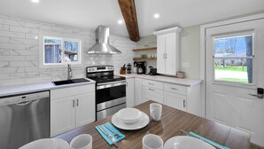 A modern kitchen with white cabinetry, a stainless steel range hood, and a wooden ceiling beam. - Cozy Beach Cottage with Sauna & Spacious Backyard just 5mins from the Beach (Port Rowan)