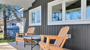 A wooden deck with two Adirondack chairs and a small table, a gray building with dark siding and white trim, and a blue covered object in the background. - Cozy Beach Cottage with Sauna & Spacious Backyard just 5mins from the Beach (Port Rowan)