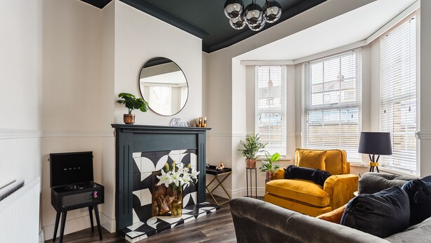 A living room with a fireplace, a sofa, a TV stand, and a window with blinds. - STUNNING 5 BEDROOM TOWNHOUSE 5 MINS TO CITY CENTRE (Lisburn)