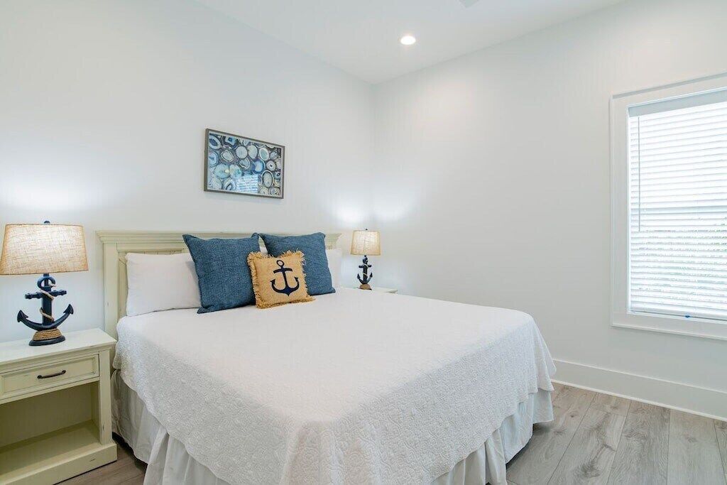 Een slaapkamer met een bed, twee nachtkastjes, een raam met zonwering en een kunstwerk aan de muur.