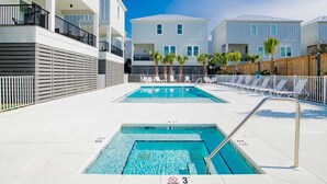 Zona de piscina con dos piscinas, una valla blanca y un edificio con balcones.