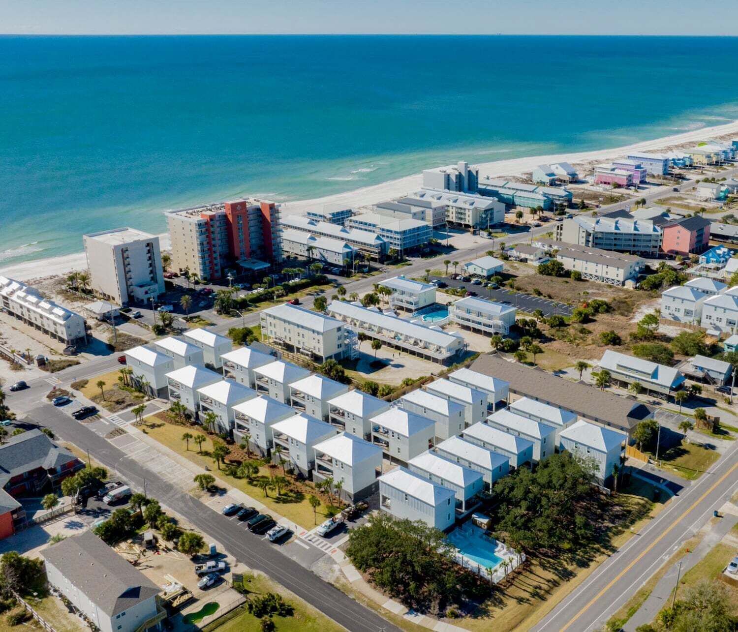 An aerial view of a coastal hotel area with multiple buildings, a beach, and a clear blue sky.