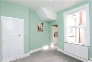 A room with teal walls, a white door, a large window, and a poster of the Golden Gate Bridge.
