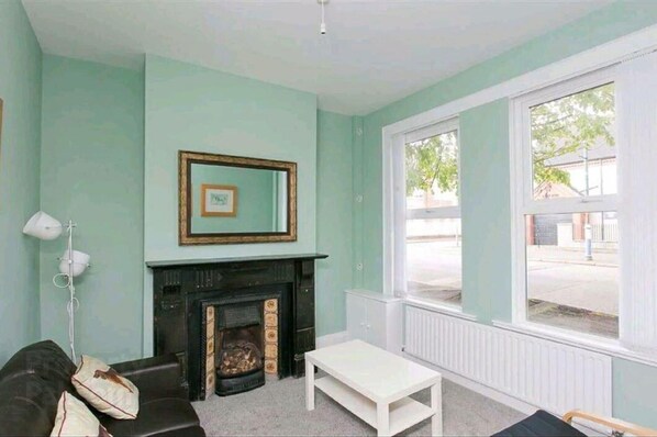 A living room with a fireplace, a framed picture on the wall, a white radiator, and a large window.