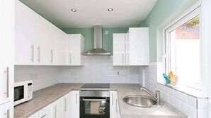 Una cocina compacta con armarios blancos, horno empotrado, microondas, pileta de acero inoxidable y una ventana que proporciona luz natural.