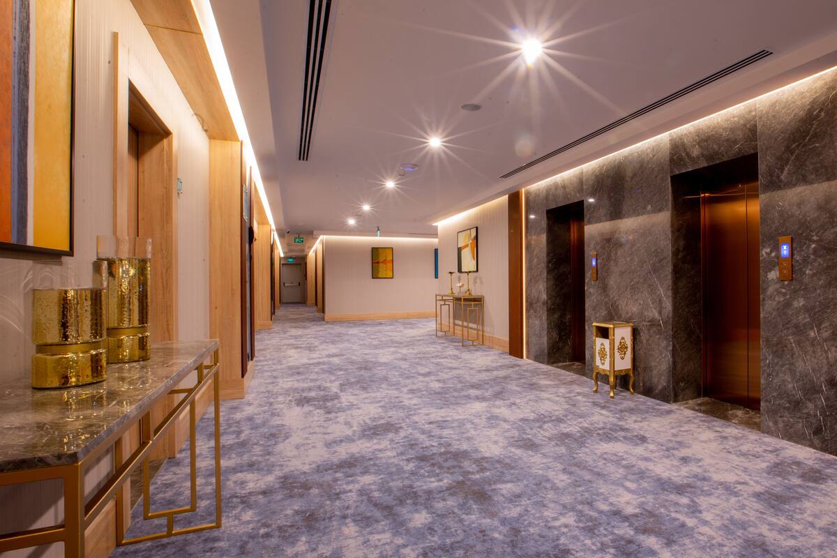 Corridoio di un hotel con pavimento in marmo, rivestimenti in legno e una reception con dettagli dorati.