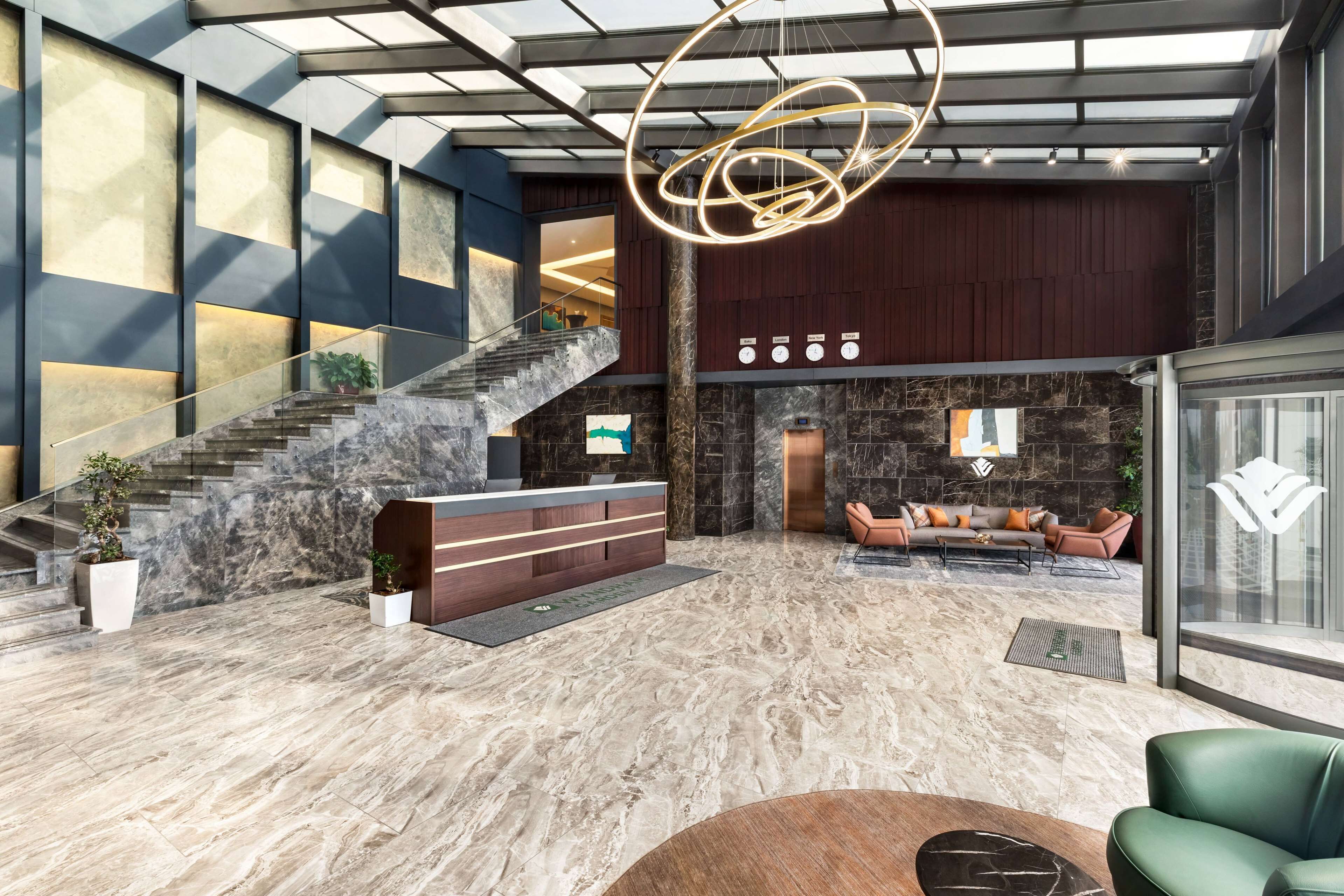 A spacious lobby with a marble floor, a reception desk, a staircase, and a seating area with a sofa and armchairs.