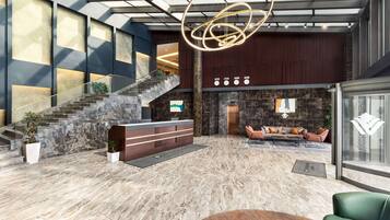 A spacious lobby with a marble floor, a reception desk, a staircase, and a seating area with a sofa and armchairs.