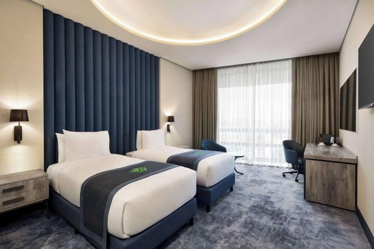 A hotel room with two beds, a desk, a chair, and a large window with curtains.