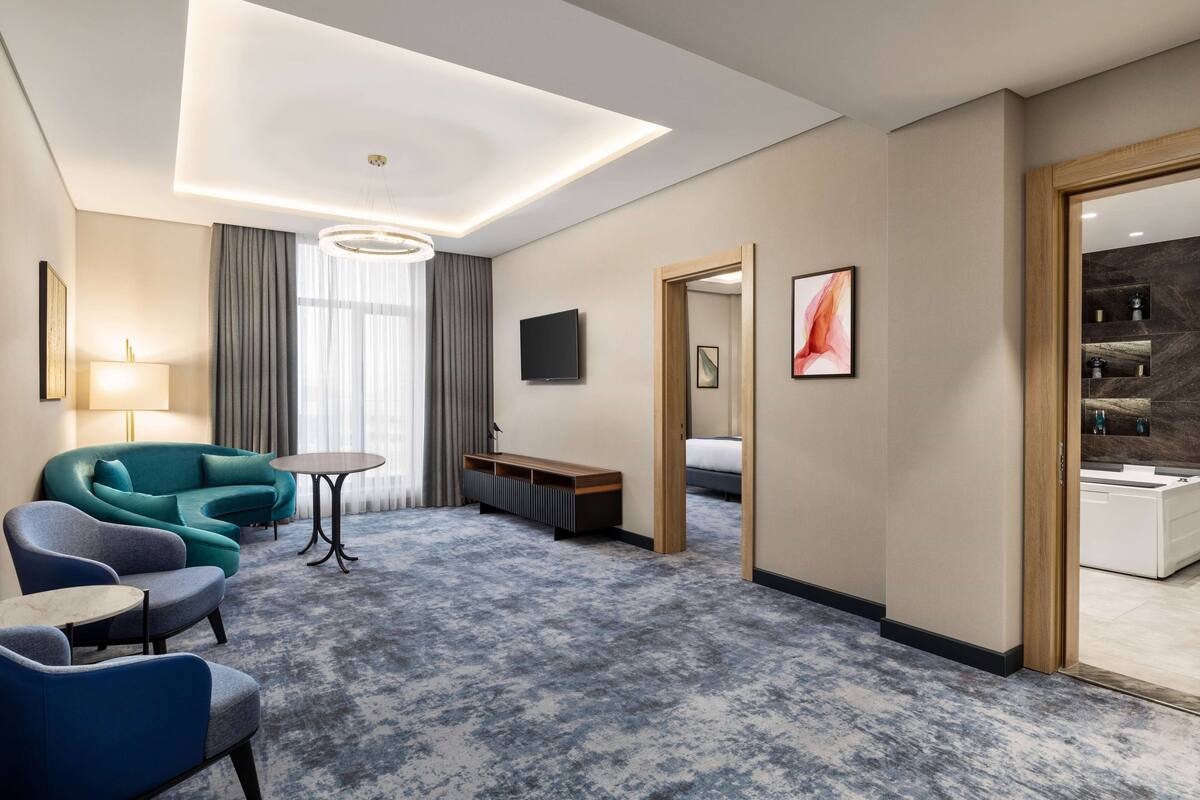 Una camera d'albergo moderna con un letto grande, un'area salotto con divano e poltrone, un tavolino e una televisione.