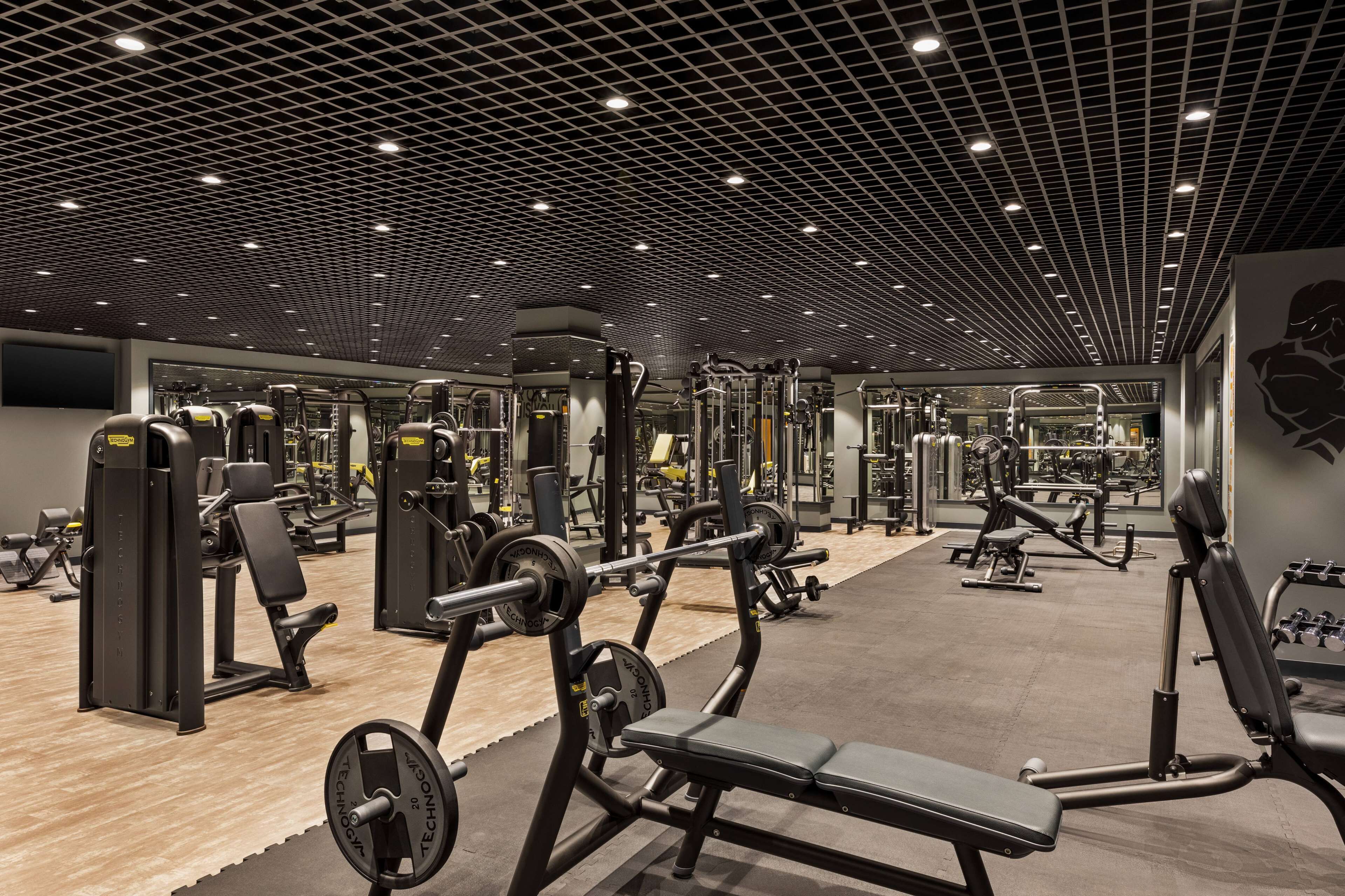 A gym with various exercise equipment, a mirrored wall, and a patterned ceiling.