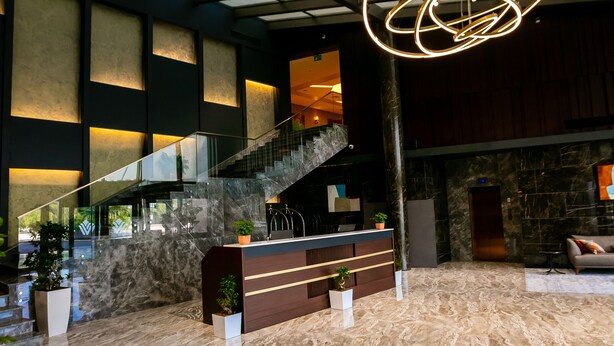 A spacious lobby with a marble floor, a reception desk, a staircase, and a large glass ceiling.