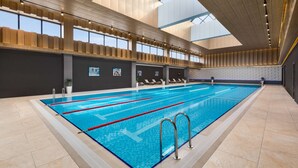 An indoor swimming pool with clear lanes, a tiled floor, and a high ceiling with natural light.