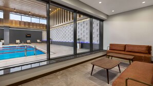 A modern indoor pool area with a glass wall, a seating area with a sofa and table, and a patterned wall in the background.
