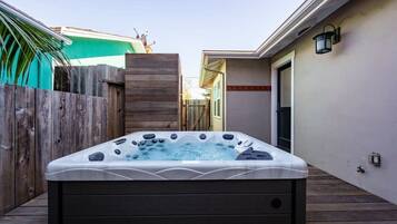 A hot tub in a backyard with a wooden deck, a wooden fence, and a house in the background.