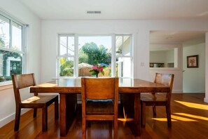 Comedor con mesa y sillas de madera, ventanas amplias y vistas a la vegetación exterior.