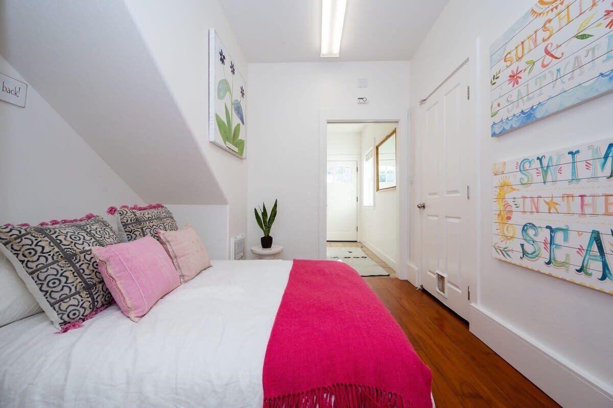 Un dormitorio con cama, almohadas, una planta y obras de arte en las paredes.