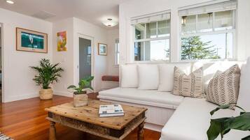A living room with a white sofa, a wooden coffee table, and a large window with white blinds.