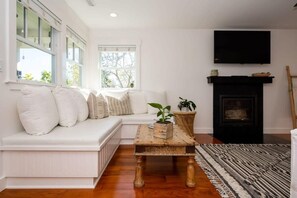 Una sala de estar con un sofá blanco, una mesa de centro de madera, una chimenea y un televisor montado en la pared.