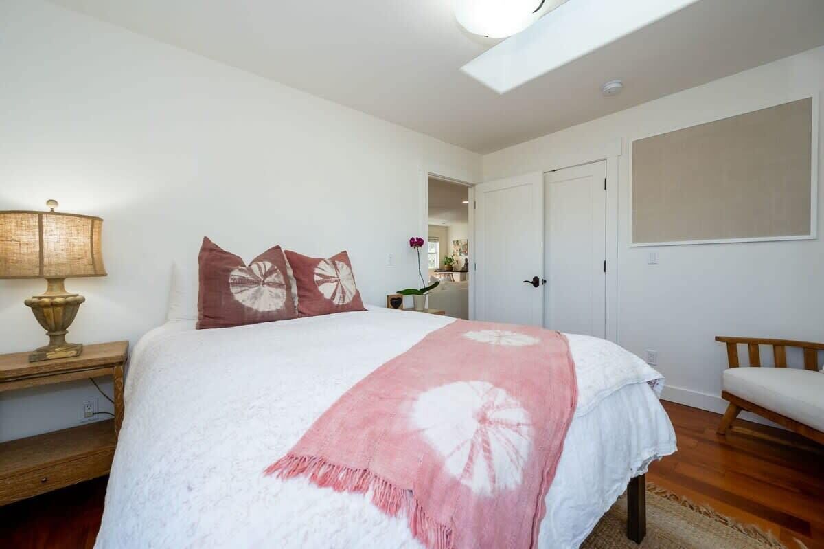 A bedroom with a bed, a bedside lamp, a chair, and a door leading to another room.