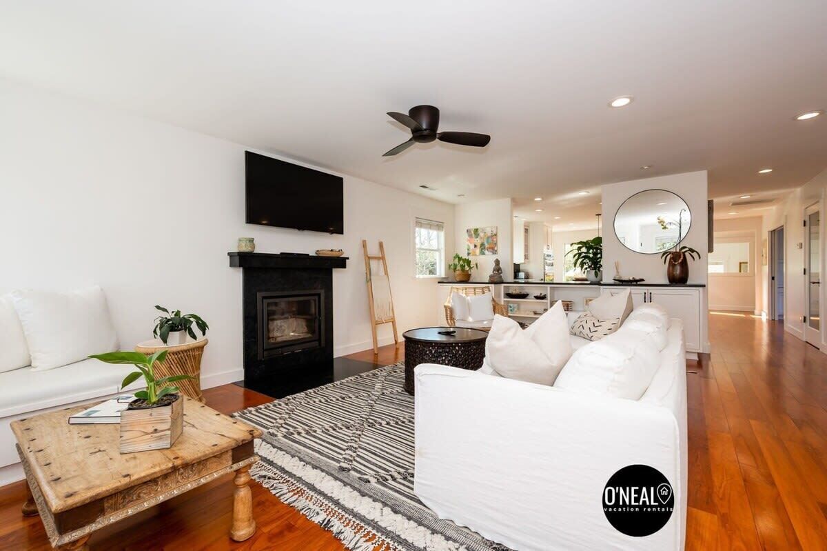 Una sala de estar moderna con chimenea, sofás blancos, una mesa de centro y un ventilador de techo.
