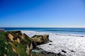 Un paisaje costero con acantilados rocosos, olas oceánicas y un cielo azul despejado.