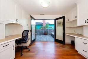 A room with a desk, chair, and open door leading to an outdoor area with a wooden deck and a potted plant.