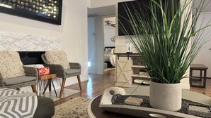 Ein modernes Wohnzimmer mit einer Couch, Sesseln, einem Couchtisch, einer Zimmerpflanze und einem Fernseher.