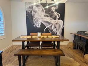 A dining area with a wooden table, bench, and a wall with a smoke-like artwork. - Cozy Home/ASU/Spring Training/Restaurants & More (Tempe)
