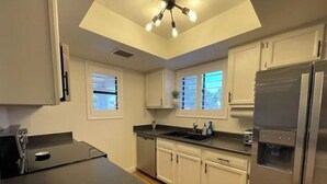Eine moderne Küche mit weißen Schränken, einem Edelstahl-Kühlschrank, einem Geschirrspüler und einer Arbeitsfläche mit Spüle.
