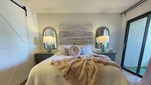 Ein Schlafzimmer mit Bett, zwei Nachttischlampen, einem großen Spiegel und Blick ins Freie.