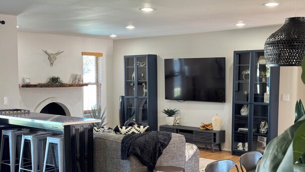 A modern living room with a kitchen area, a large flat-screen TV, and a dining table with chairs. - Cubs Stadium in backyard/Heated Pool /Dog Friendly (Mesa)
