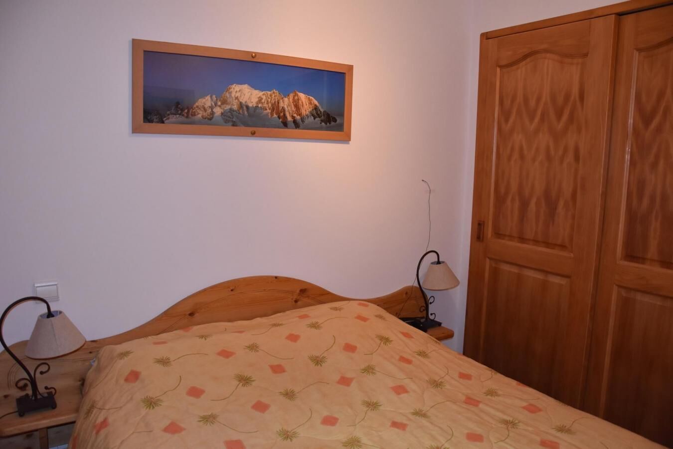 Une chambre à coucher avec un lit en bois, une table de chevet avec une lampe, une armoire en bois et un tableau encadré au mur.
