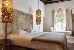 A bedroom with a large bed, a wooden headboard, a hanging light fixture, and a view of a bathroom with a bathtub. - LOOK NO FURTHER! Gorgeous old finca with sea view! (Sant Joan de Jabritja)