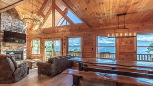 Una cabaña de madera espaciosa con chimenea de piedra, amplios ventanales con vistas a la montaña y un comedor con bancos.