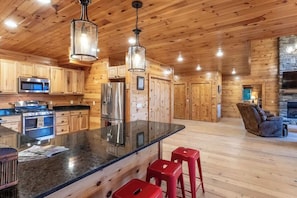 A spacious kitchen with wooden cabinets, a central island with stools, stainless steel appliances, and a stone fireplace.